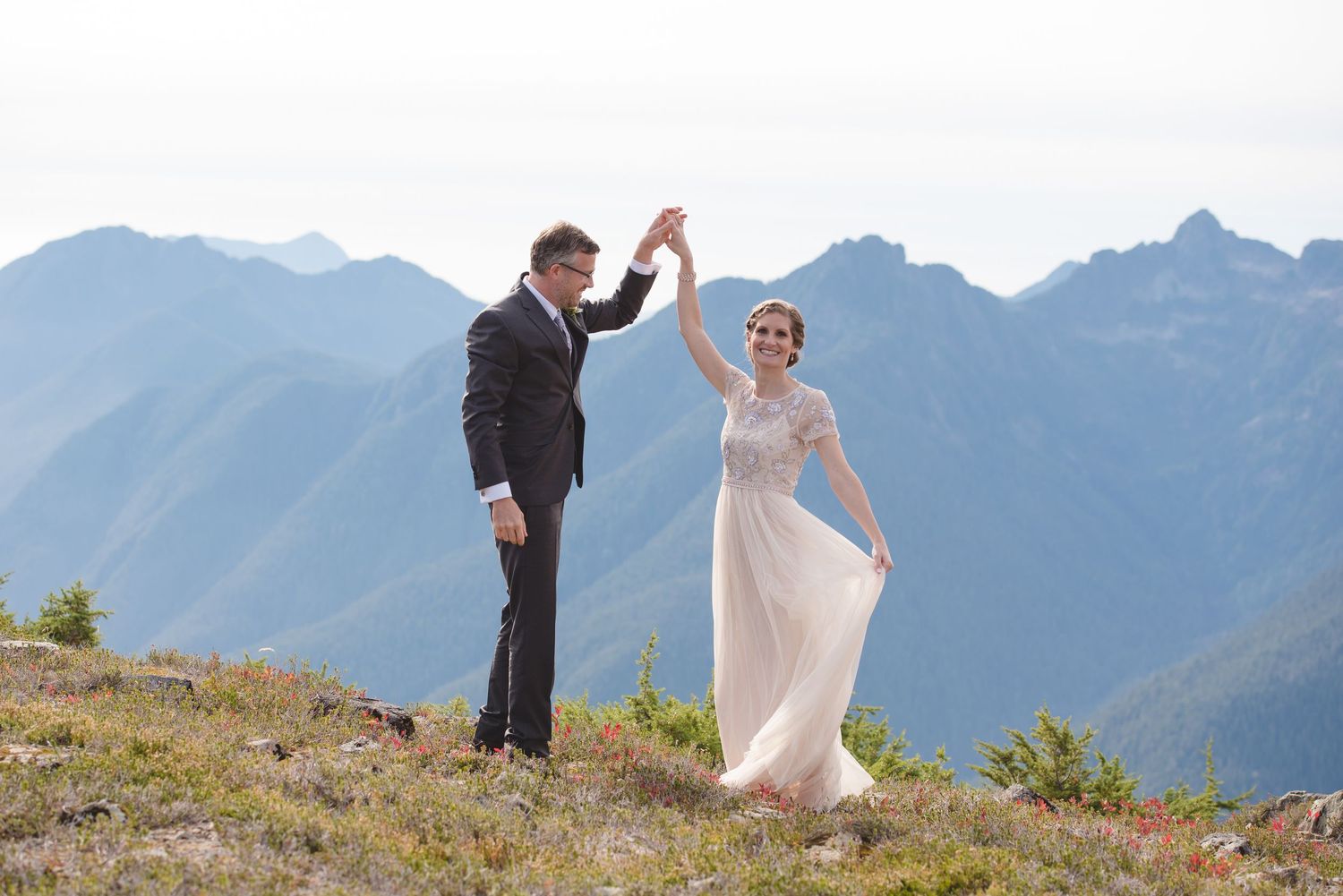 Dancing on mountain ridge with majestic alpine peaks in background.