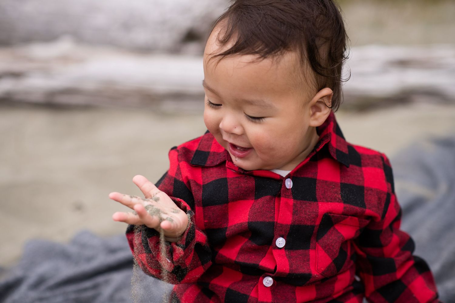 Child in red buffalo plaid shirt smiling and playing outdoors.