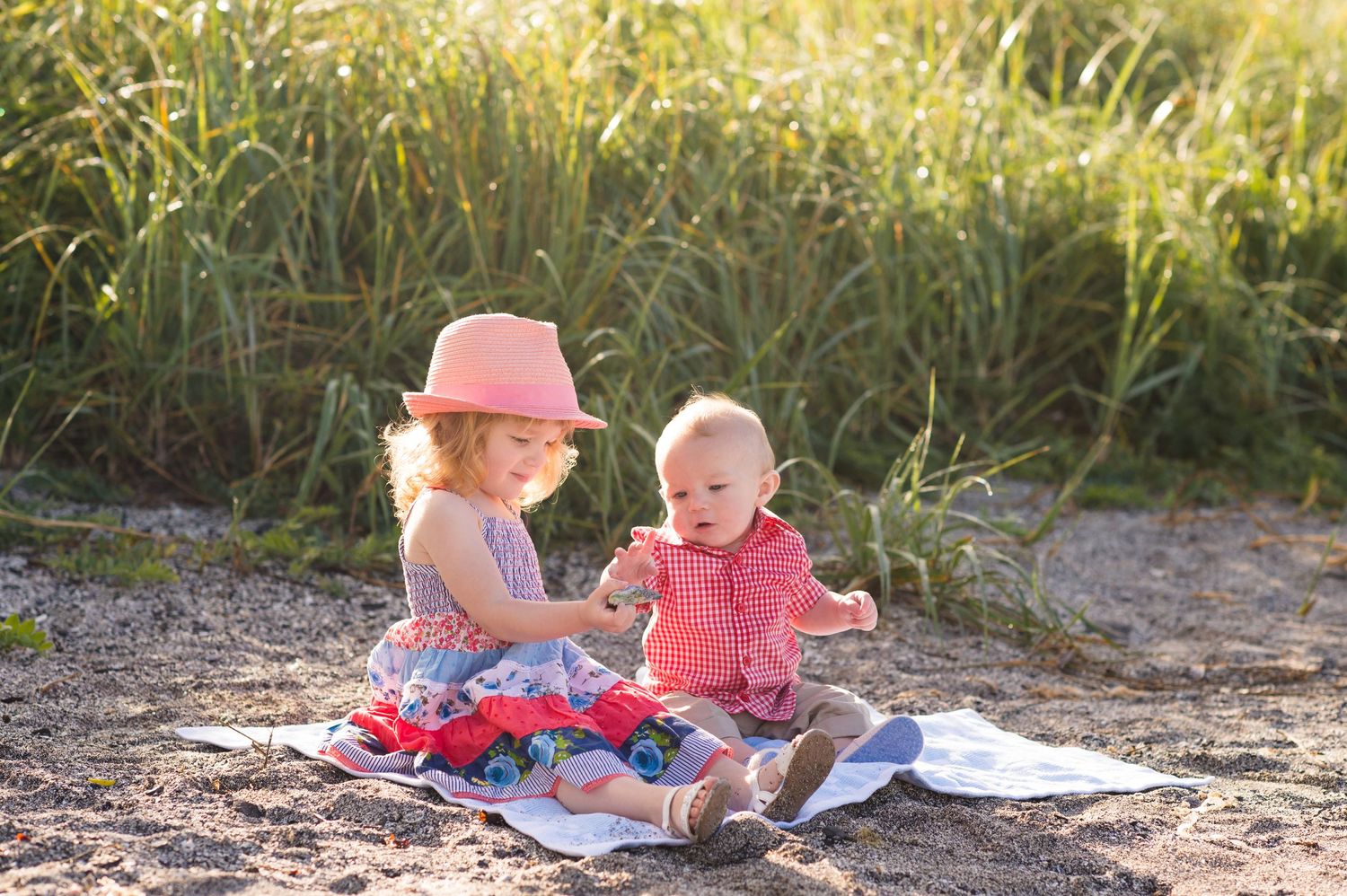 Children playing and reading together on blankets in a grassy outdoor setting during golden hour.