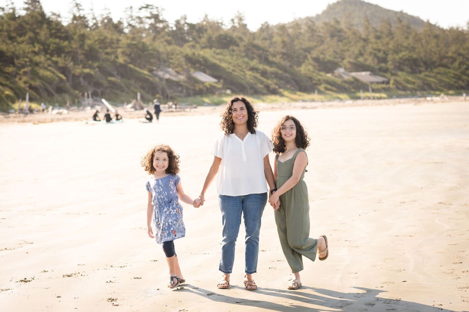 Family walking together on beach path with mountain and forest backdrop.
