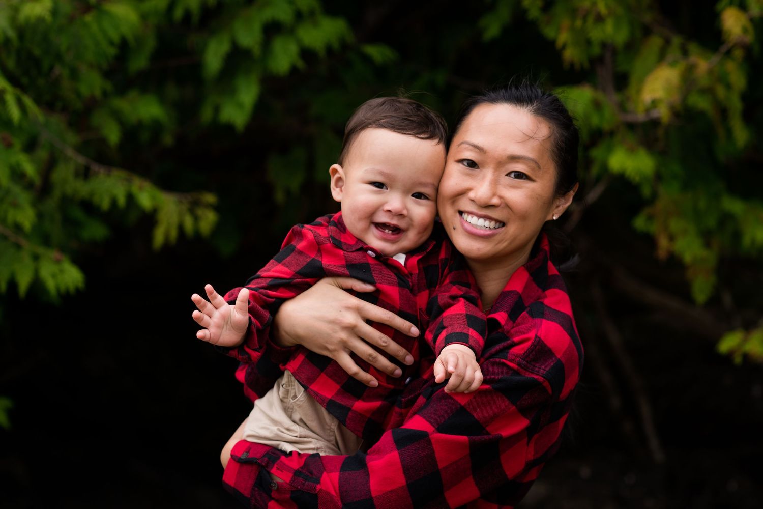 Family wearing red plaid shirts embracing outdoors against dark background.