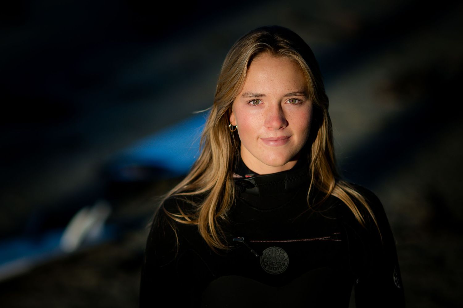 A person wearing a black wetsuit stands in dramatic lighting against a dark background with a blue glow.