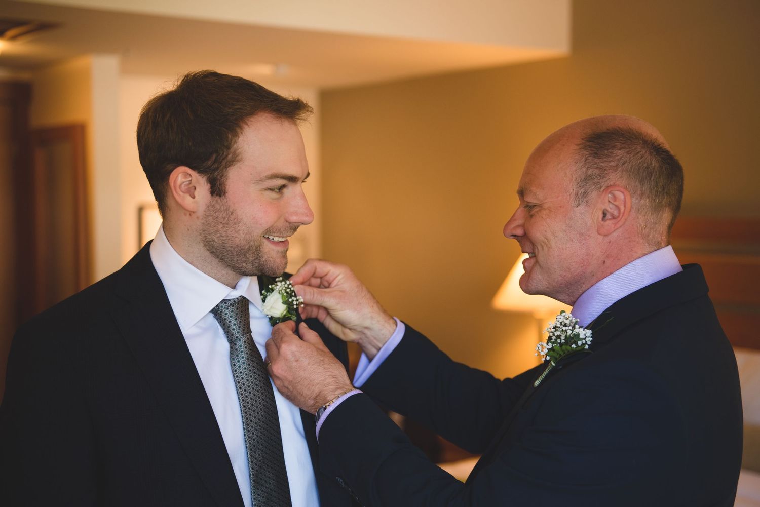 Men in dark suits share emotional moments during wedding preparations.