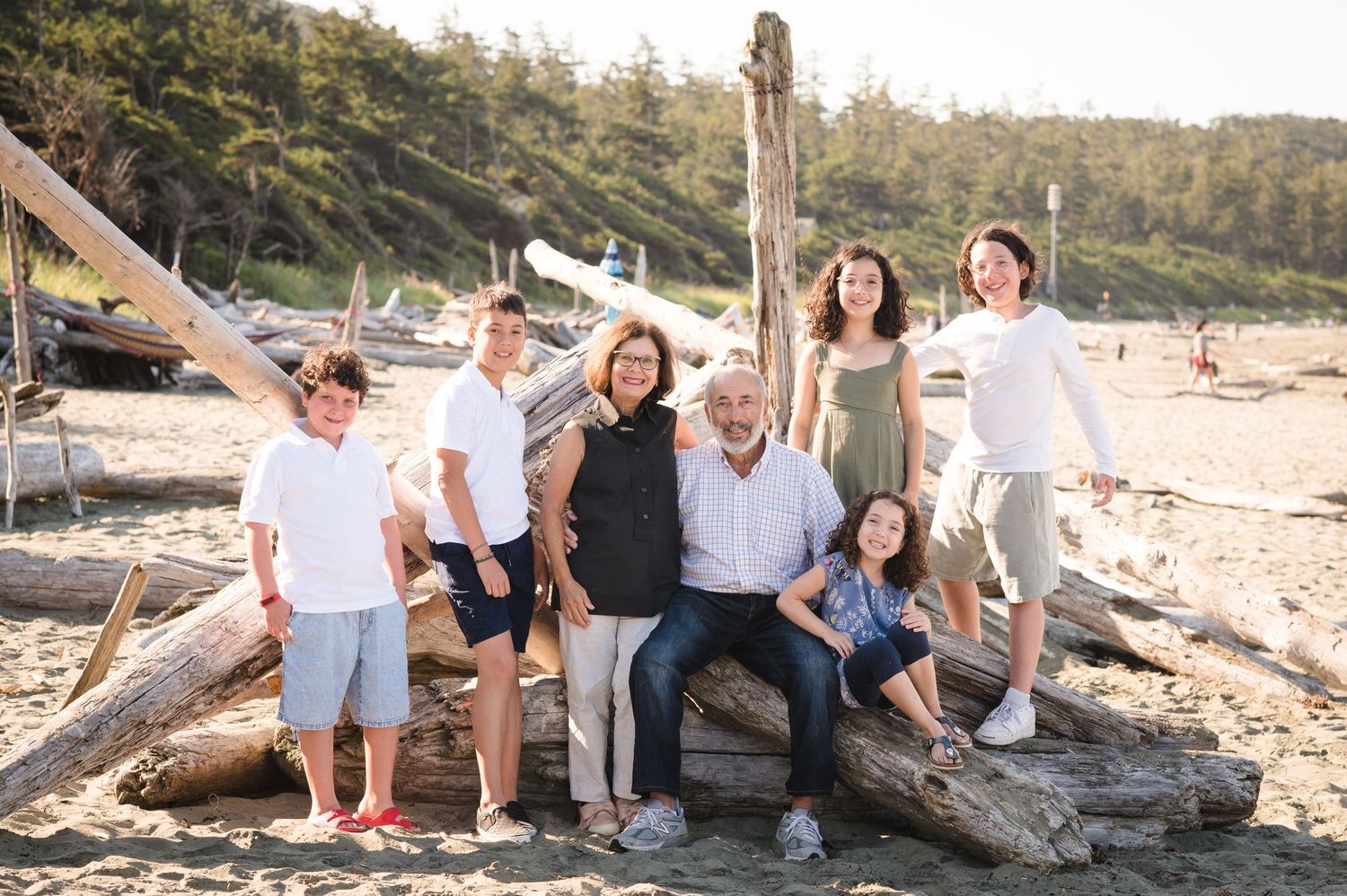 Family group sitting casually on driftwood at a scenic beach during golden hour.