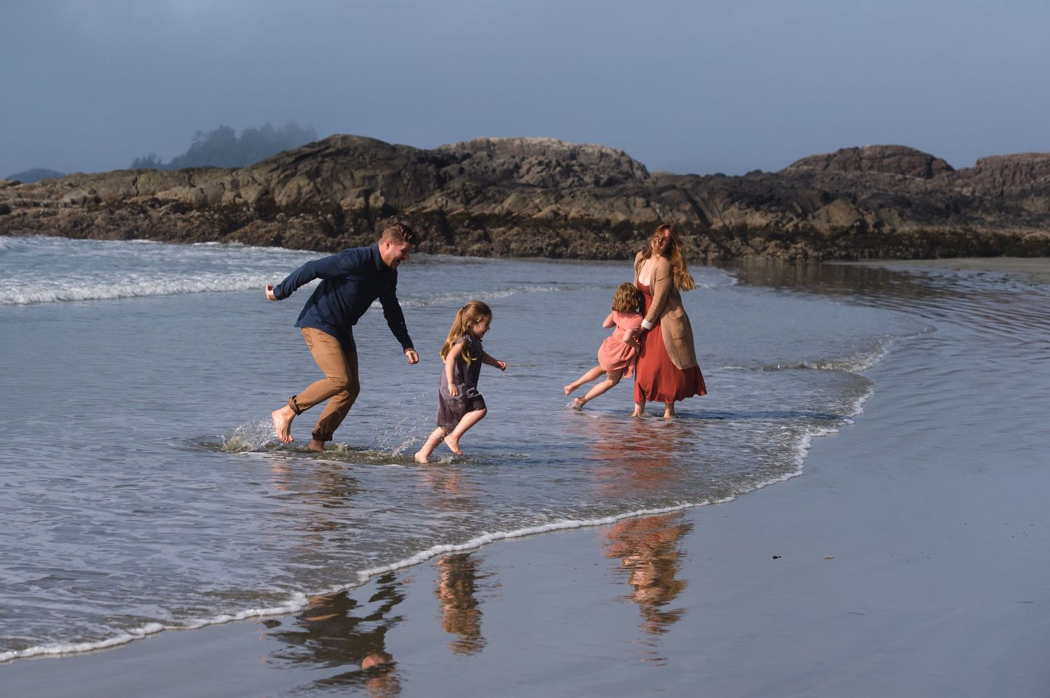 People splashing and playing in shallow ocean waves near a rocky beach.