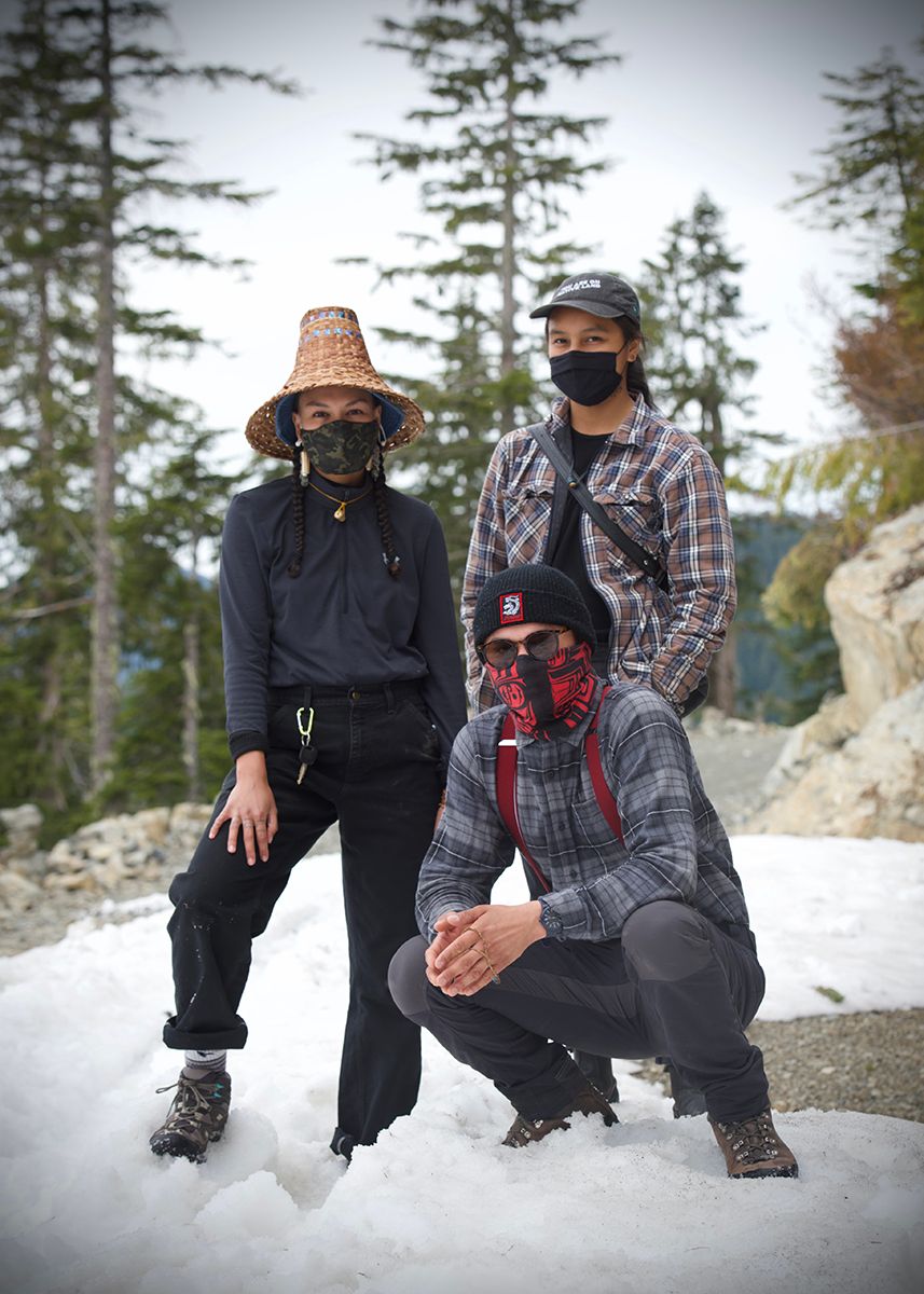 Fairy Creek blockade. Three masked individuals pose in winter gear and woven hats on snowy ground.