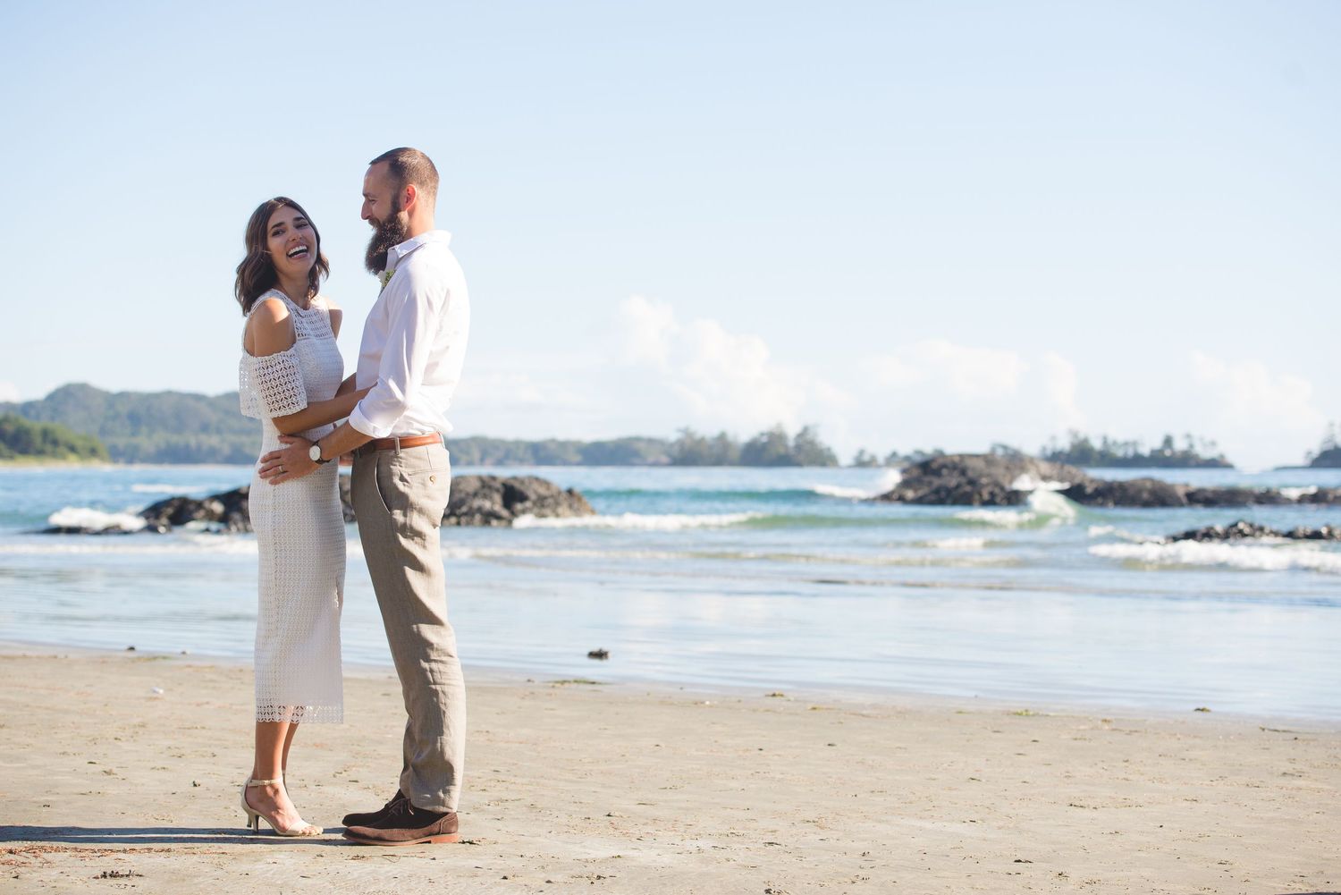 Romantic beach engagement photos with couple posing together on sandy shore at sunset.