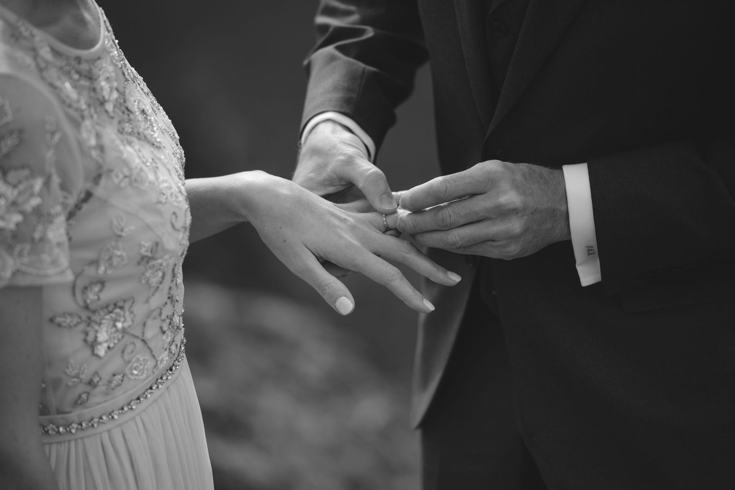 Black and white detail shot of hands exchanging rings during wedding ceremony.