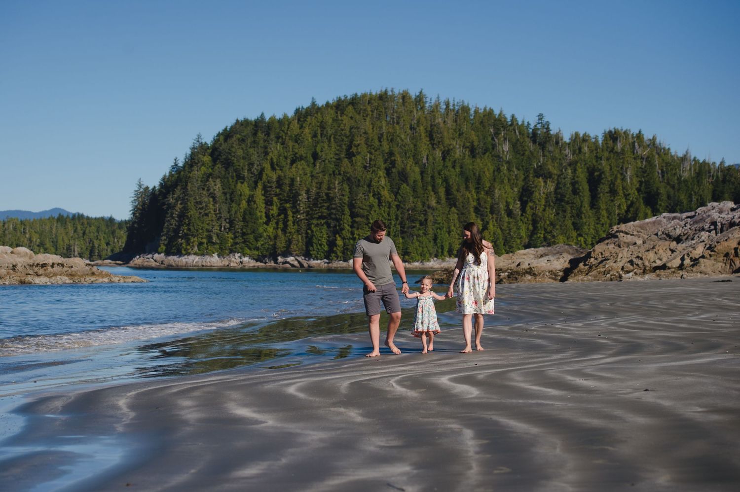 Wide landscape view of a rocky beach with forested islands in the distance.
