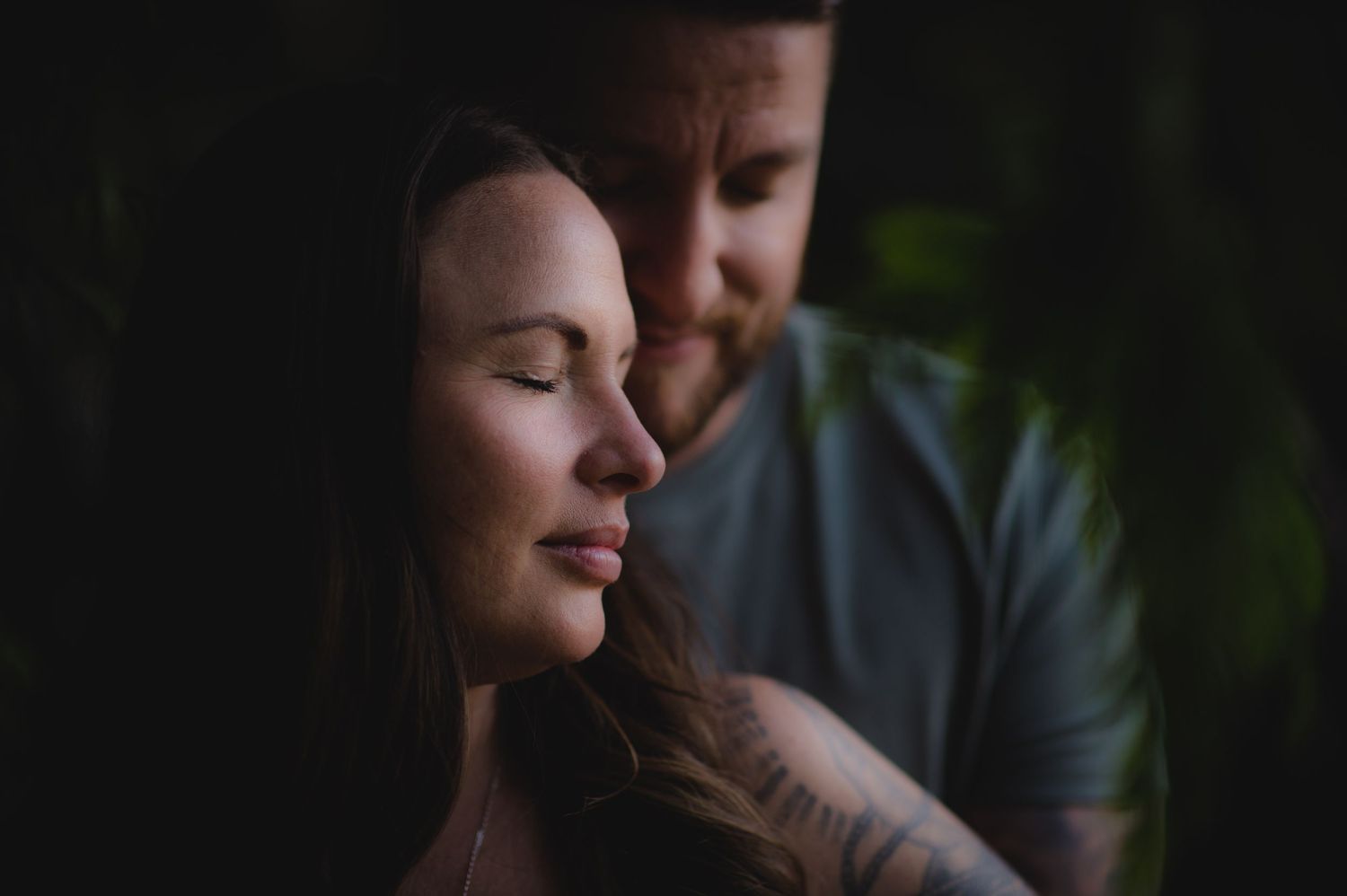 An intimate black and white portrait of a couple in a romantic forest setting.