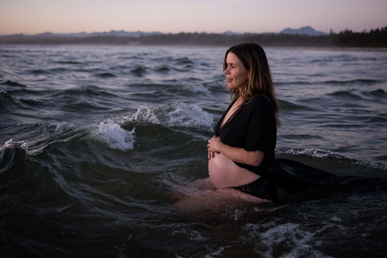 Person in black dress floating in moody ocean waters during sunset.