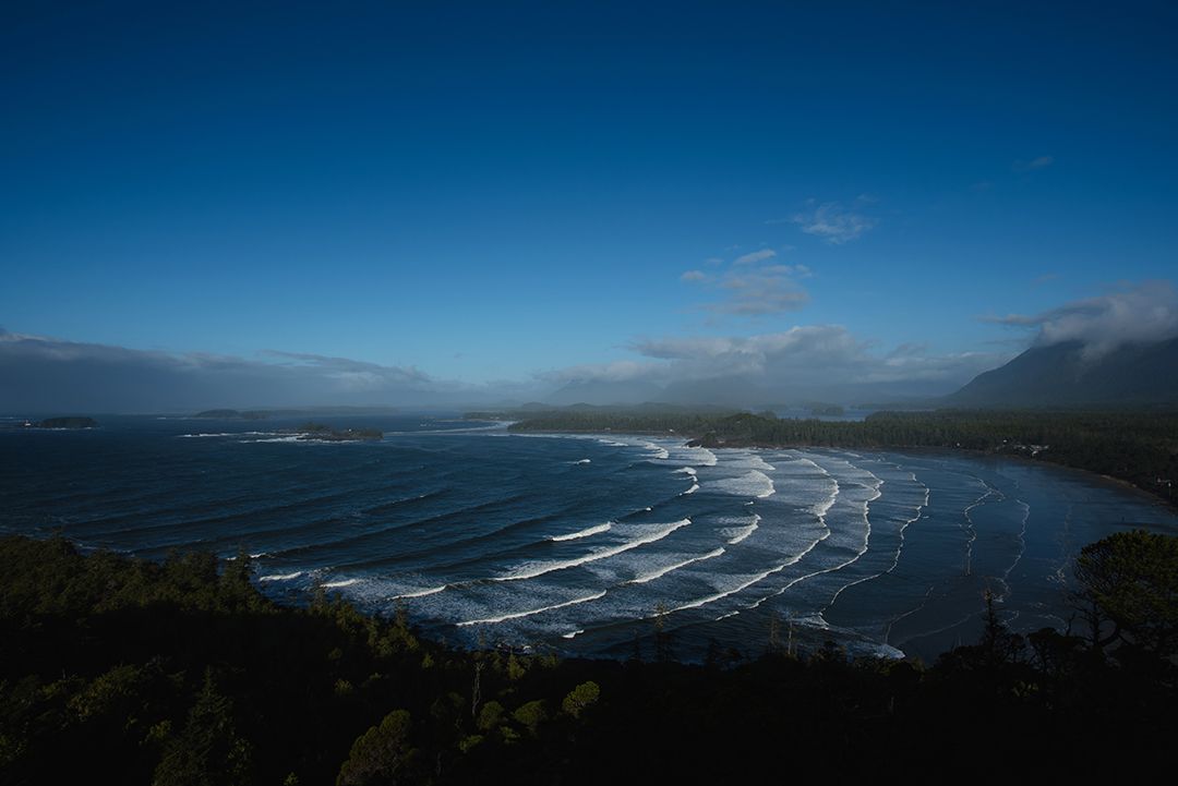 Panoramic aerial view of a rugged coastline with rolling waves under a deep blue sky.