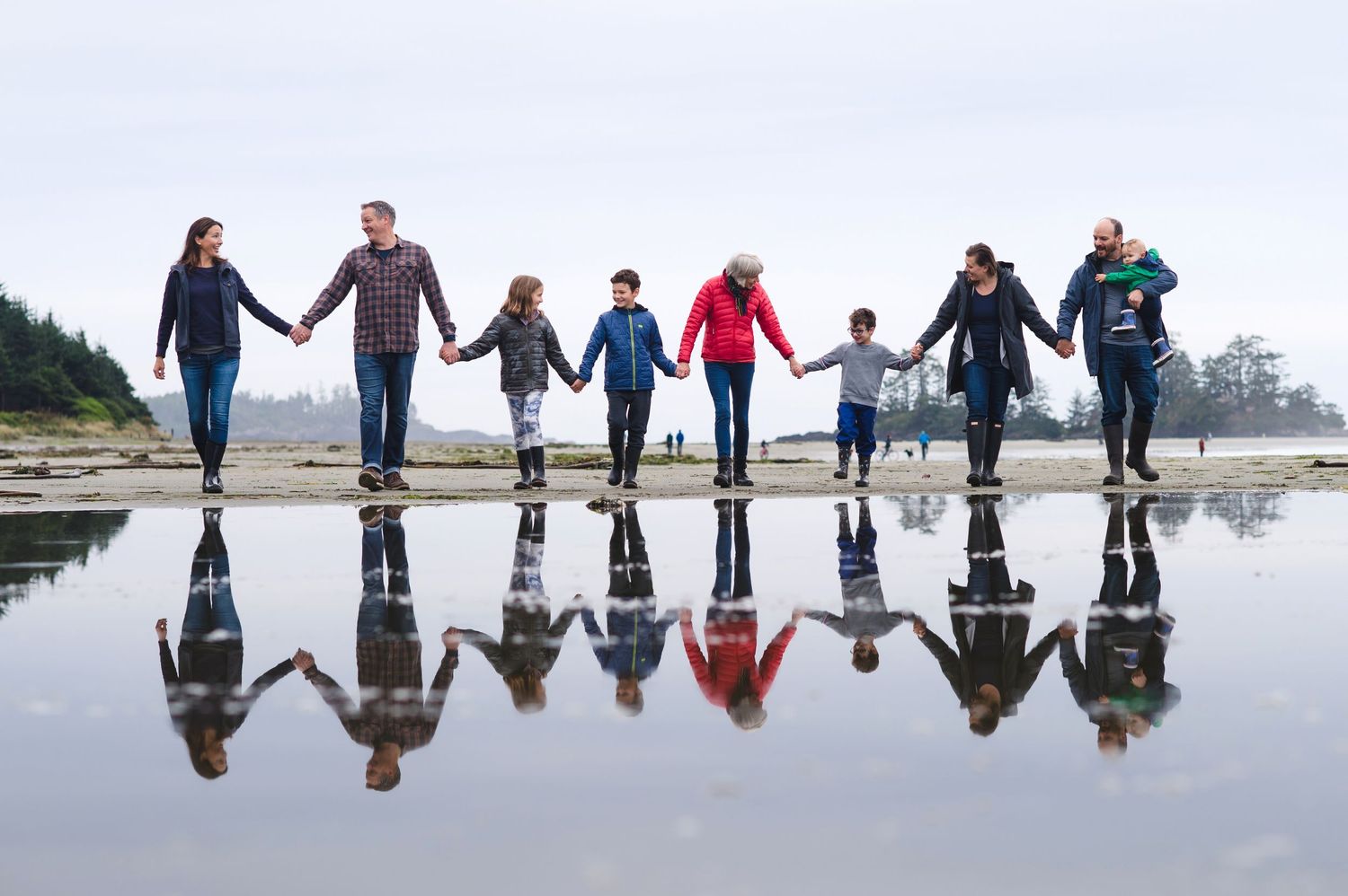 Creative reflection photo of group holding hands on wet beach sand during low tide.