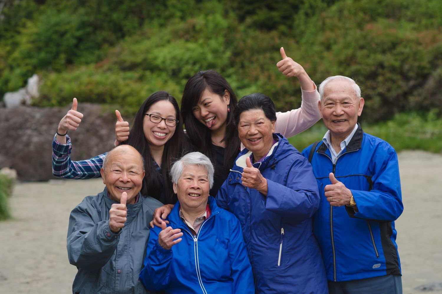 Group of seniors in blue jackets giving enthusiastic thumbs up gestures outdoors.