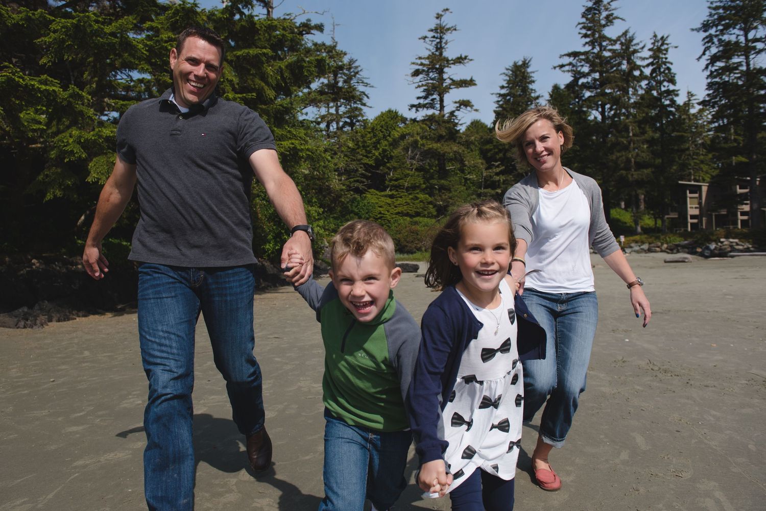People walking together on a sandy beach with evergreen trees in the background during a sunny day.