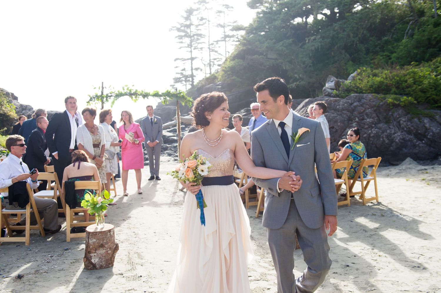 Wedding party poses for photos on a scenic beach path surrounded by evergreen trees.