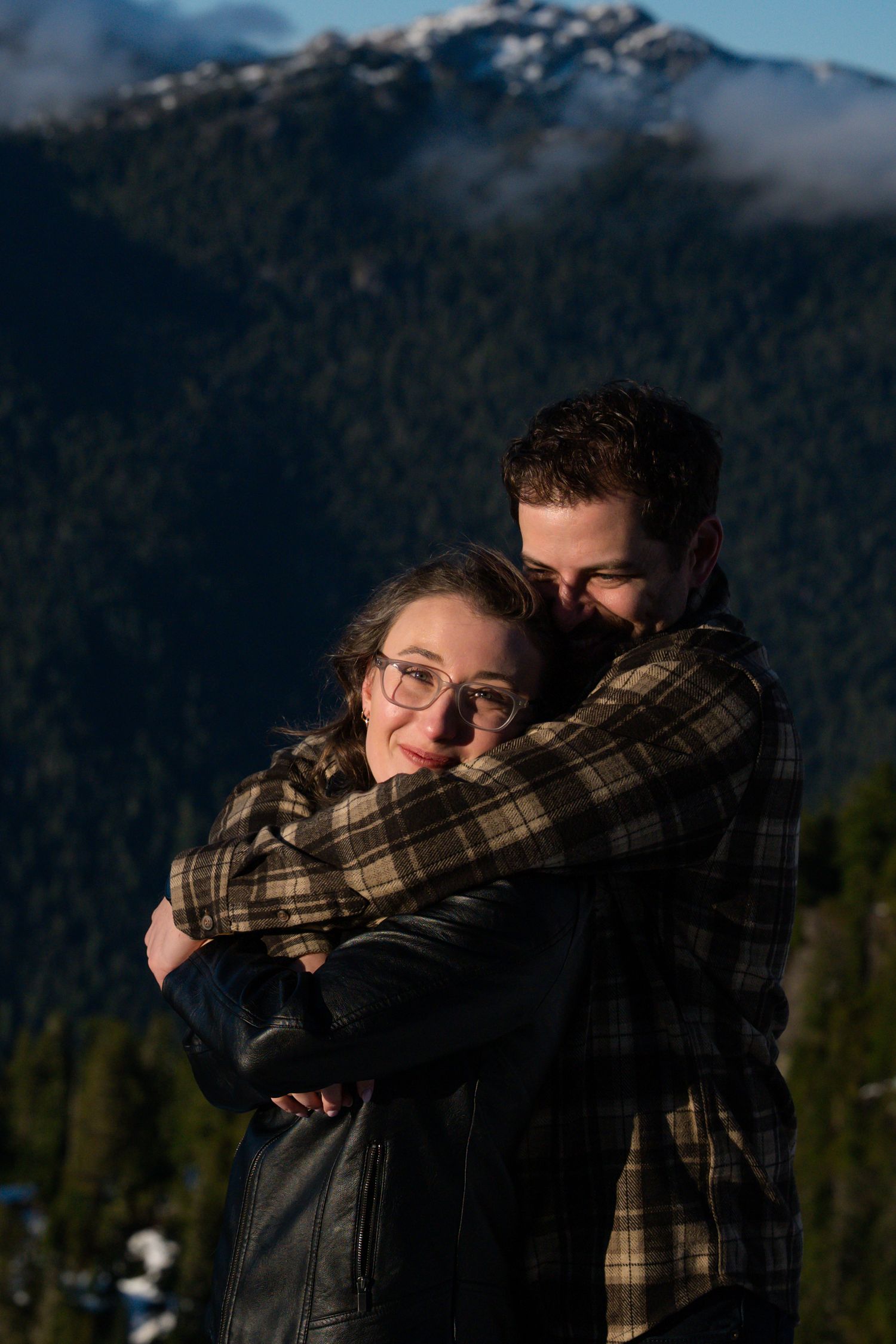 Couple embracing warmly with stunning snow-capped mountain backdrop during golden hour engagement shoot.
