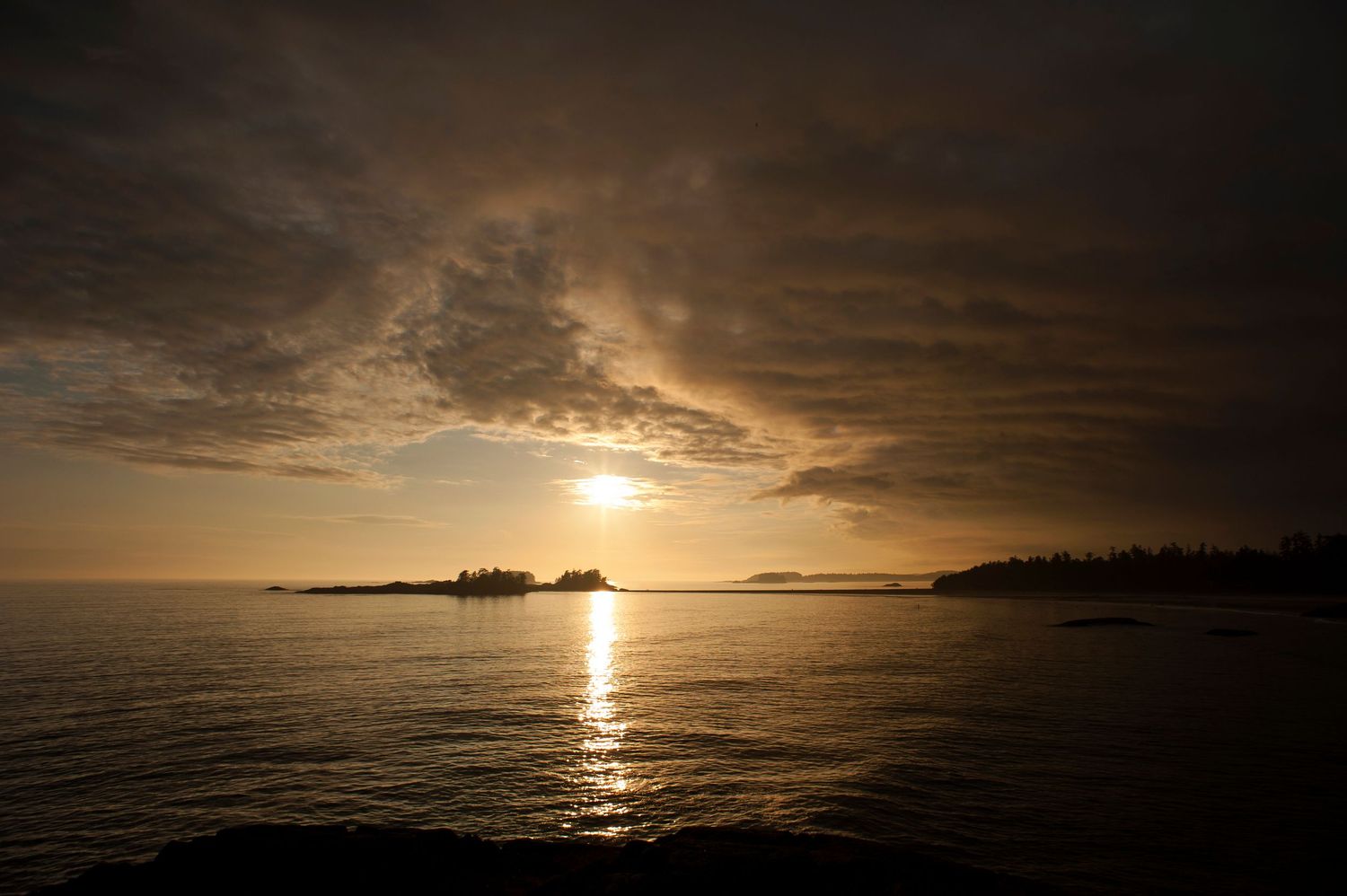 Dramatic sunset seascape with sun breaking through dark clouds over ocean horizon.