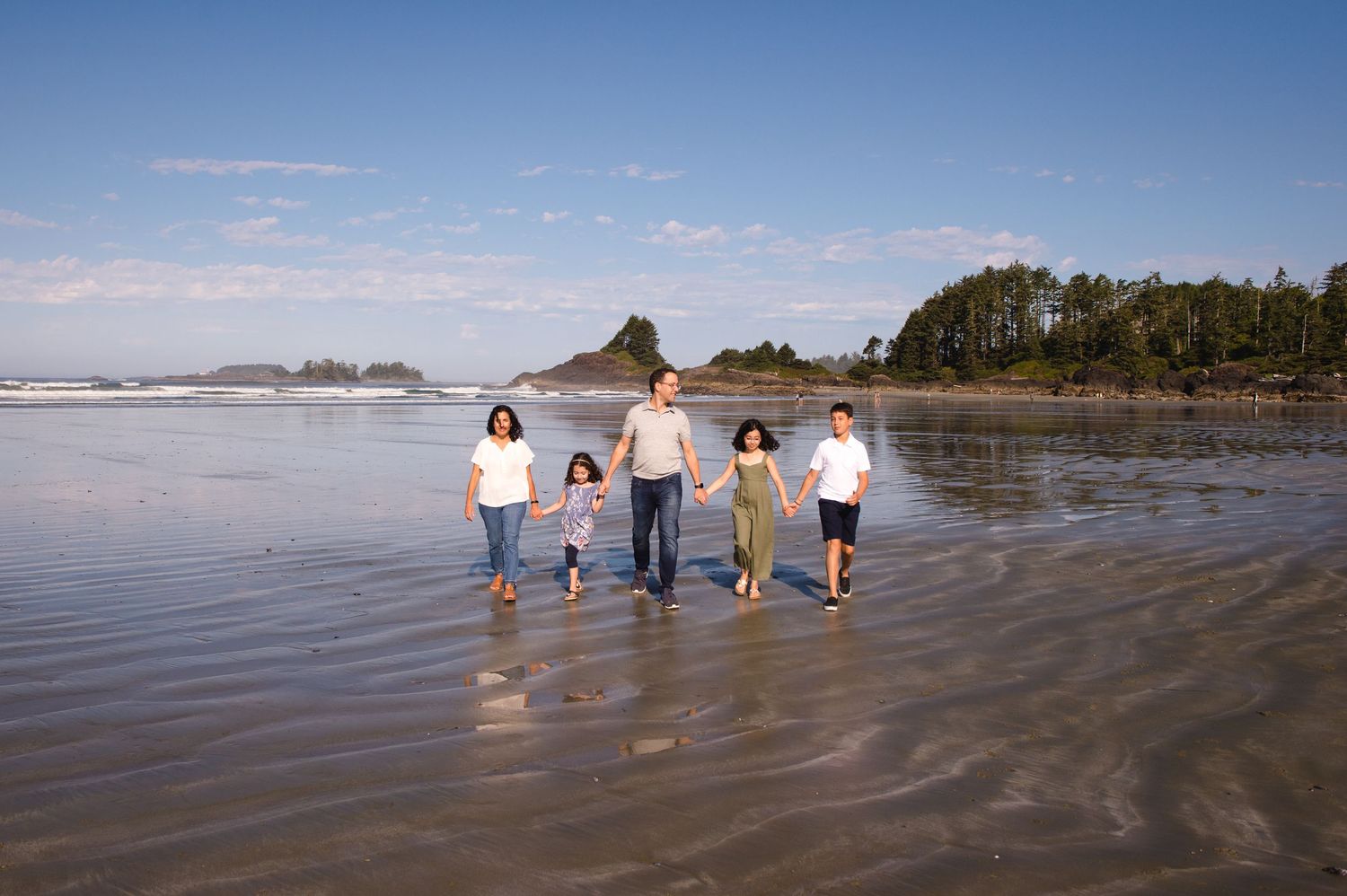 Family members walking and playing together along the shoreline on a sunny beach day.