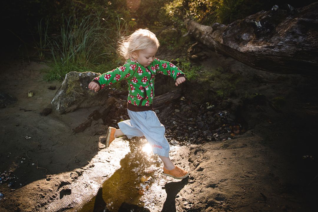 A toddler explores a sunlit forest trail while wearing a colorful patterned shirt on a summer day.