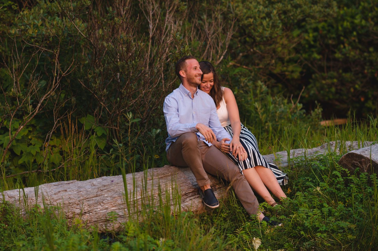 Couple enjoying a romantic moment on a grassy hillside overlooking the ocean during golden hour.