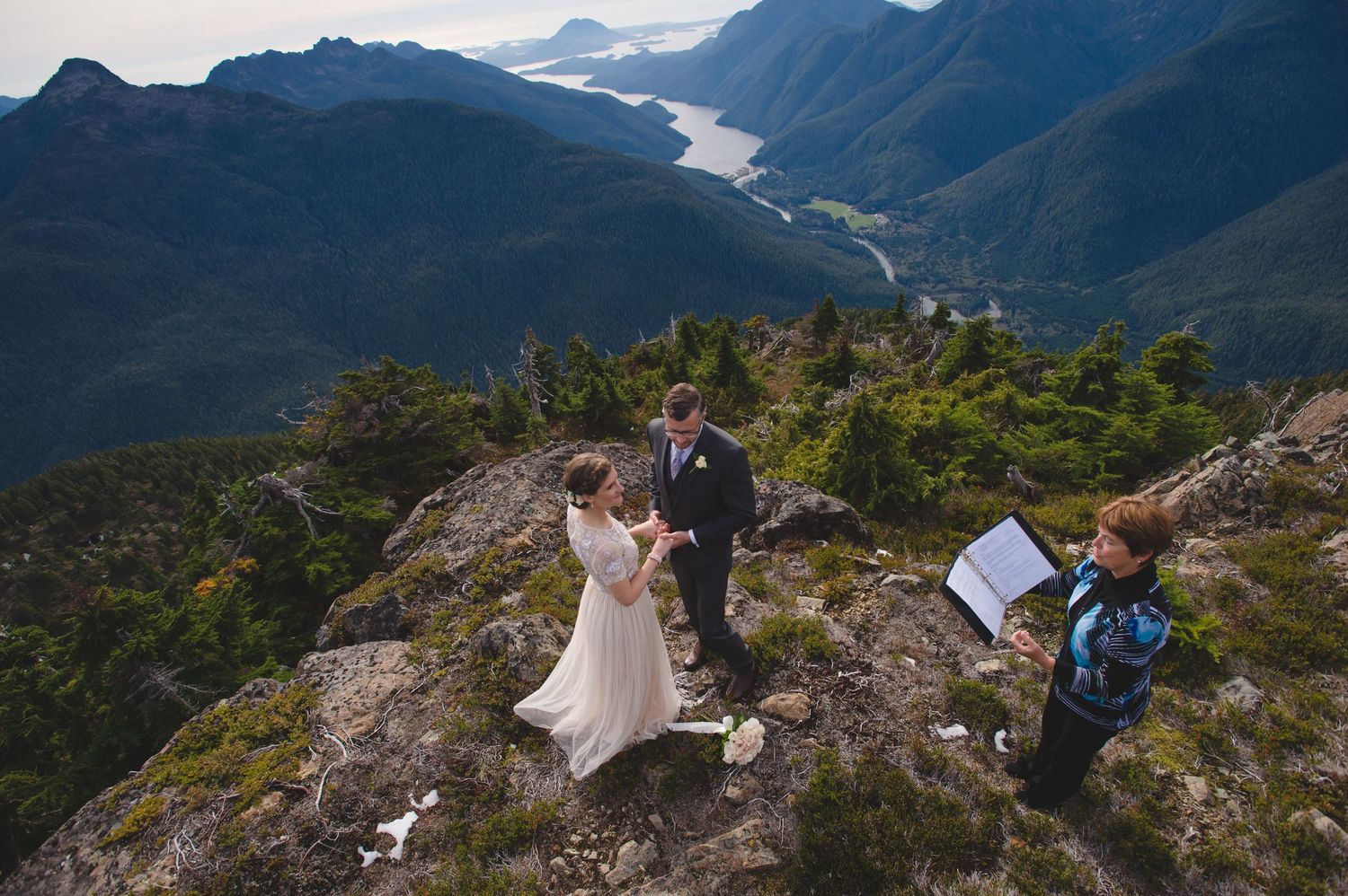 Panoramic view of a mountain wedding ceremony with dramatic coastal fjords in the background.