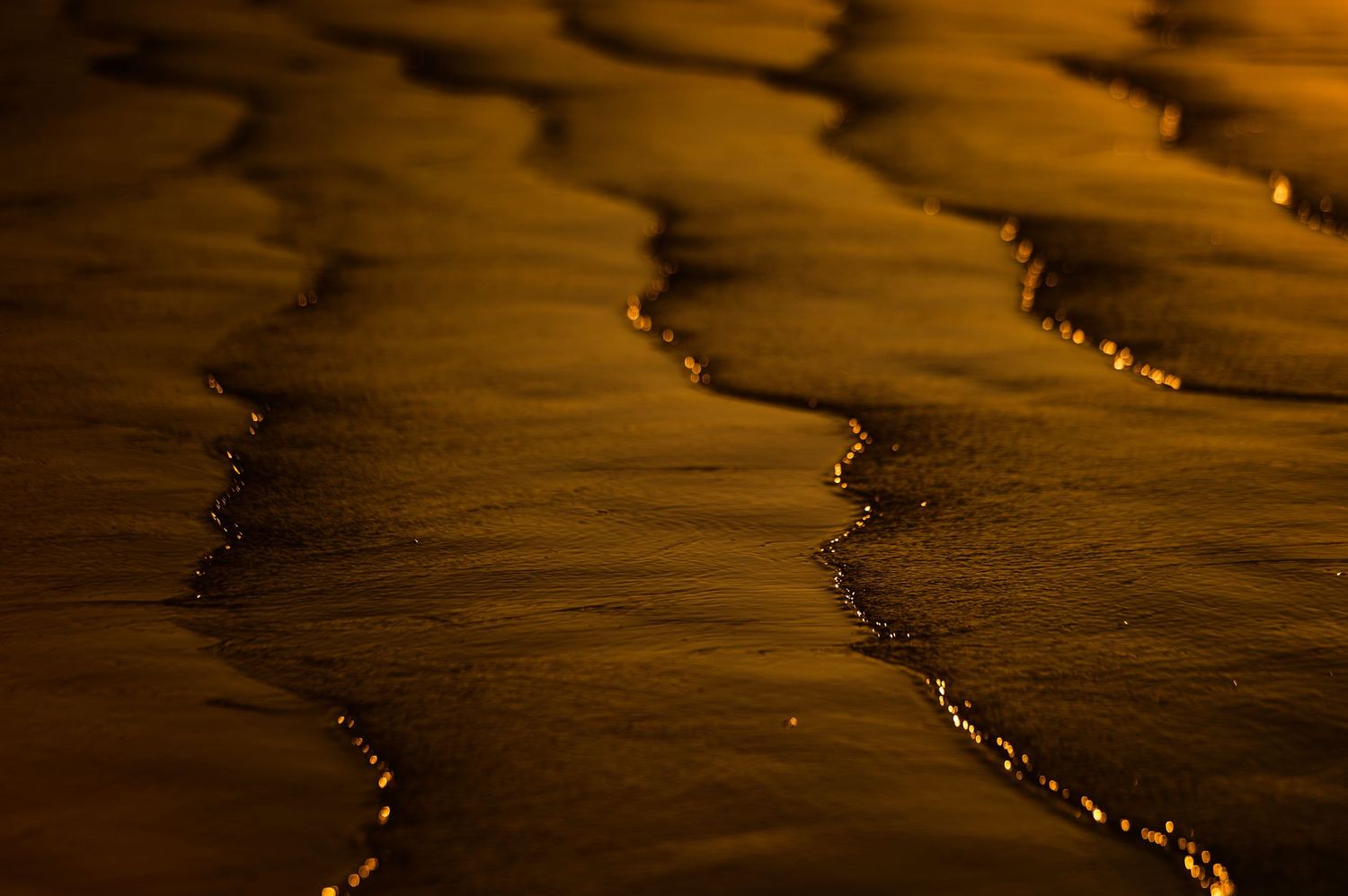 Abstract patterns of golden sunlight reflecting on rippling beach water at sunset.