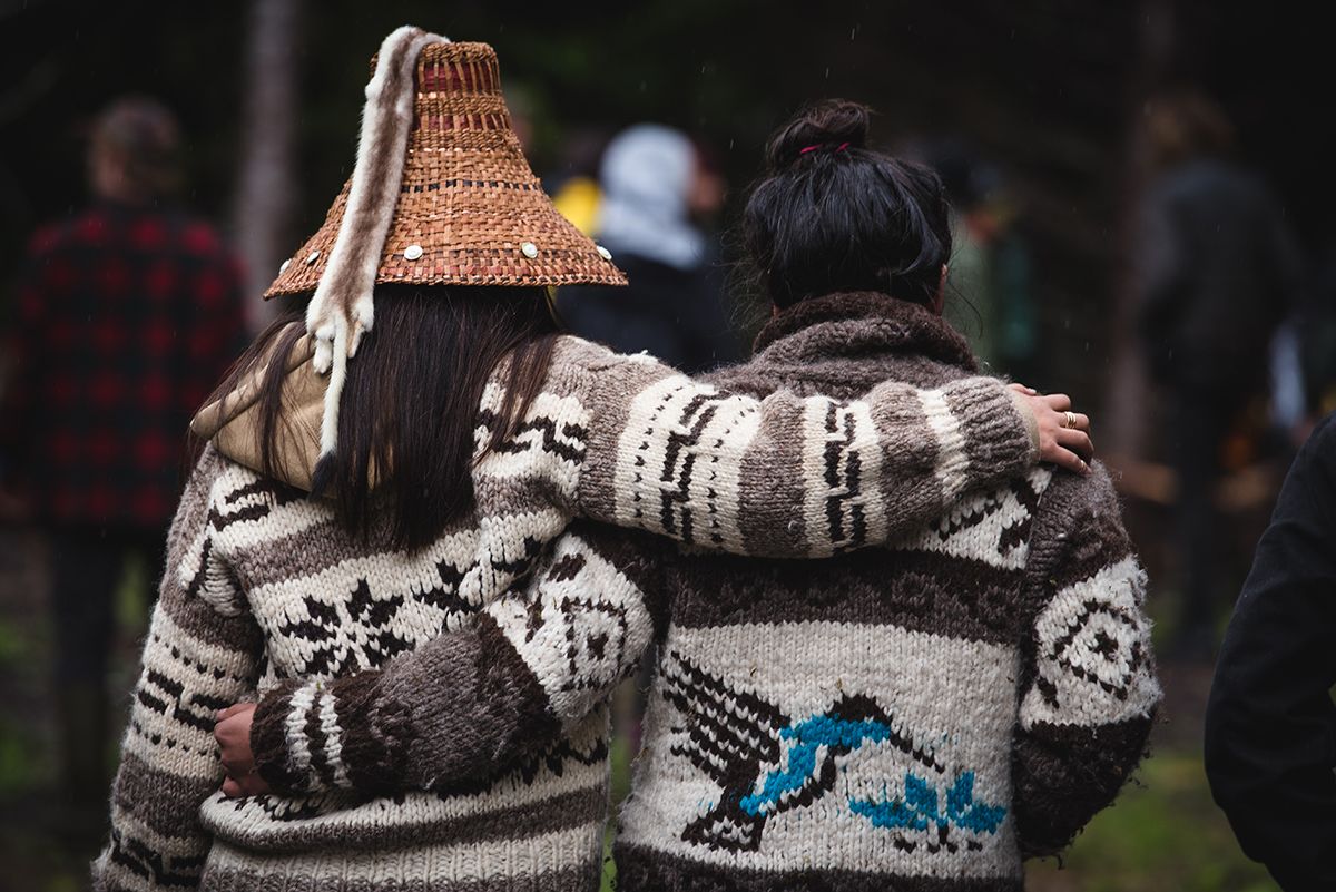 Fairy Creek blockade. Two people wearing cozy patterned sweaters and a woven hat stand close together outdoors.