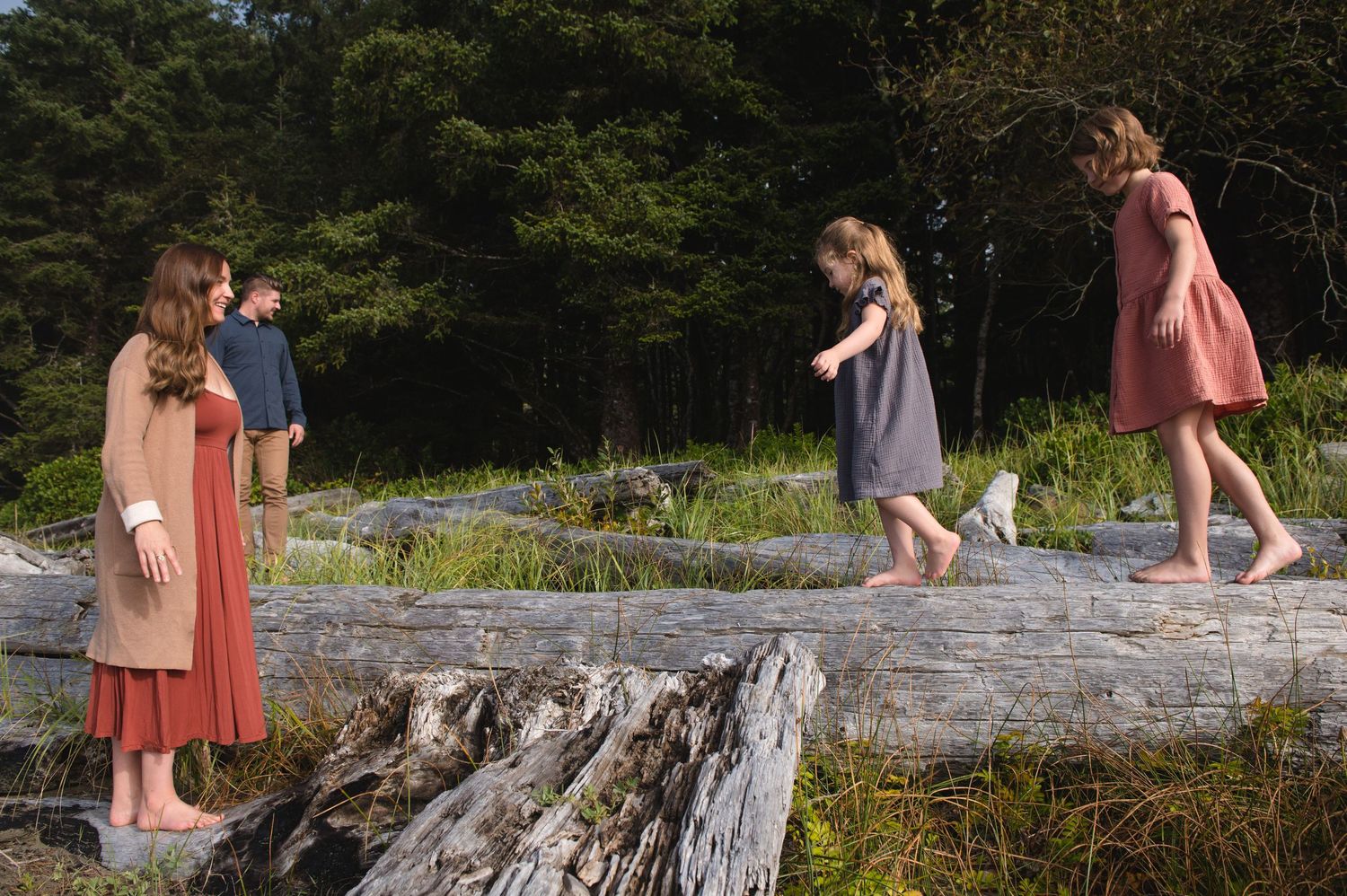 Family members playing and posing on driftwood during a beach photoshoot.