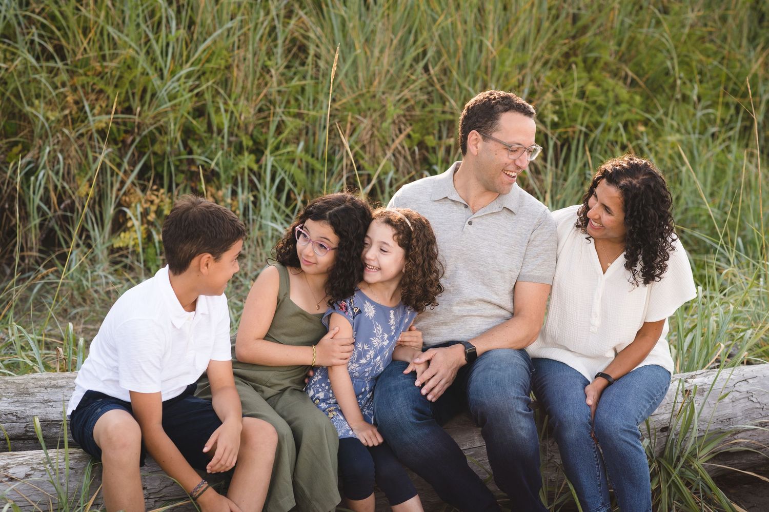Casual outdoor family portrait with everyone sitting on driftwood at the beach.