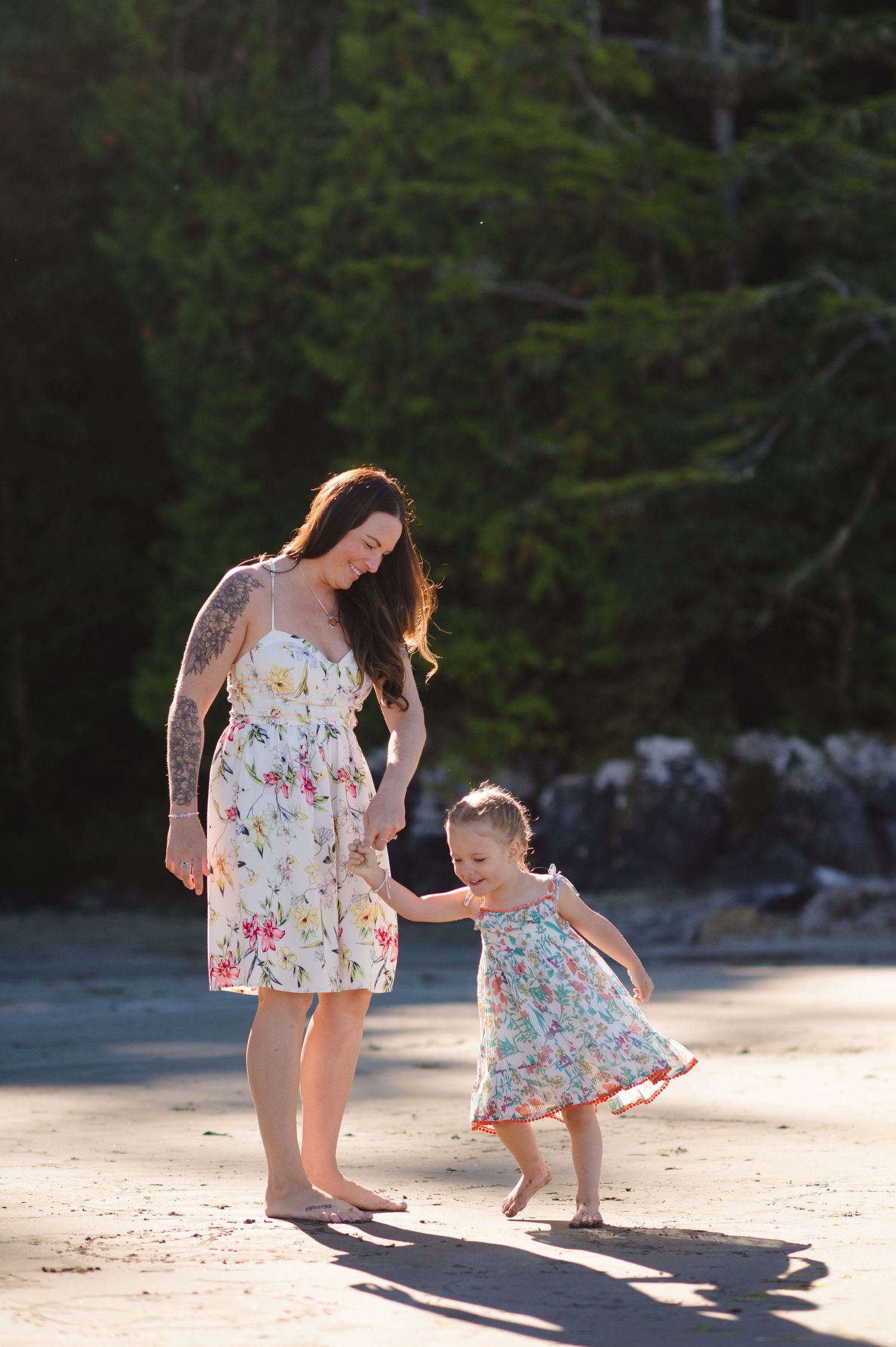 A parent and child in matching floral dresses play together on a sunny beach.