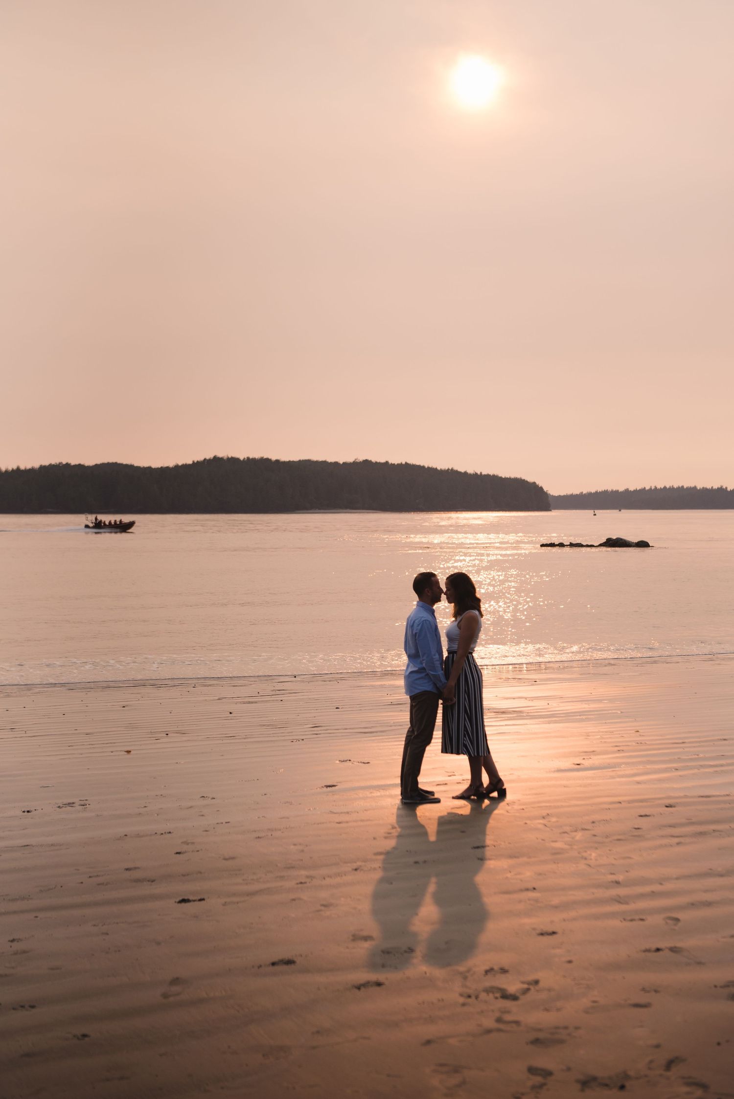 Silhouettes of a couple walking along a beach at sunset with golden light reflecting on the wet sand.