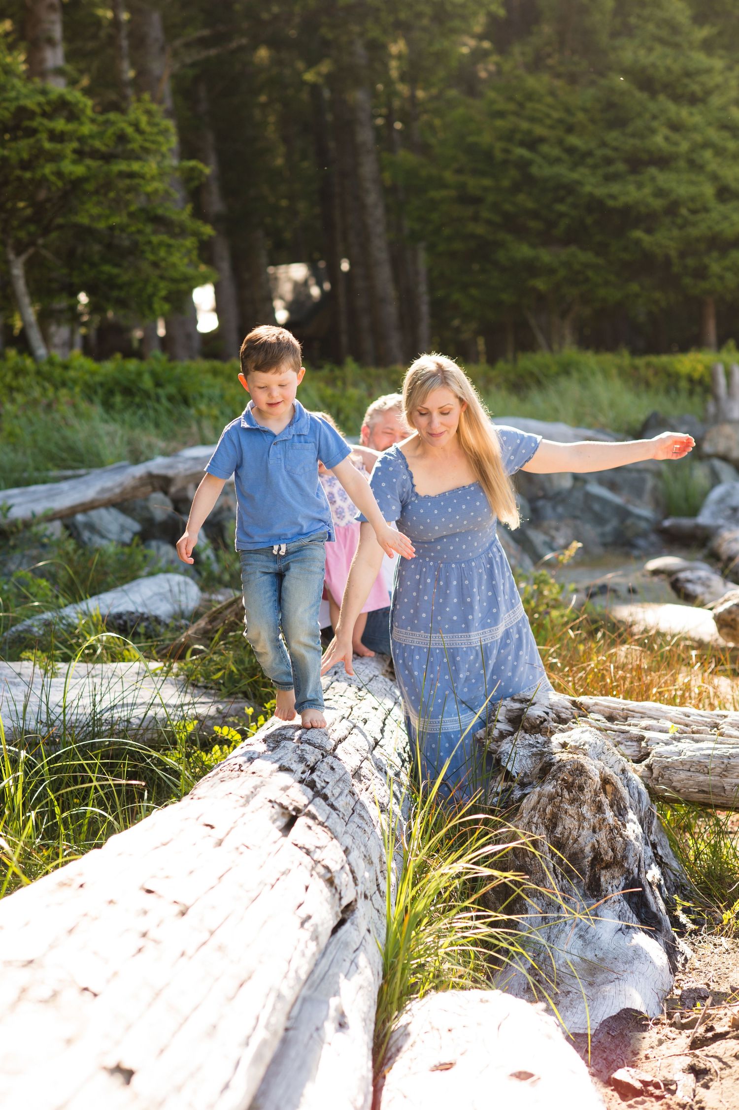 People walking together on fallen logs at a beach with forest in background during golden hour.