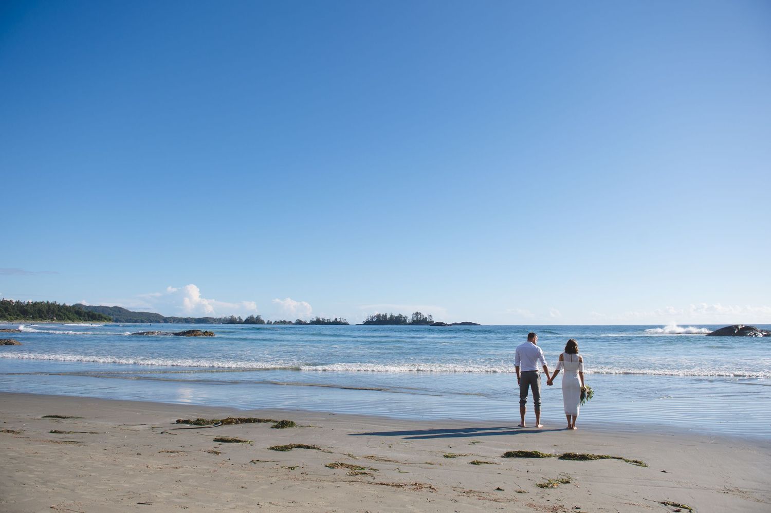 Long sandy beach stretches along Pacific coast with blue water and islands visible in distance.