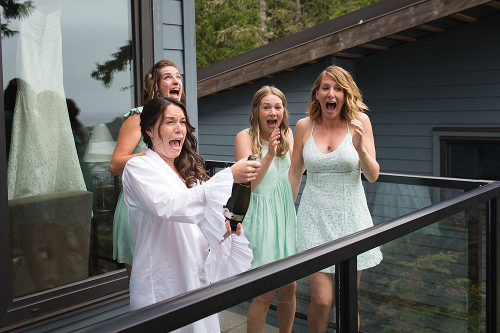 Wedding party members celebrate joyfully on an outdoor deck with trees in the background.