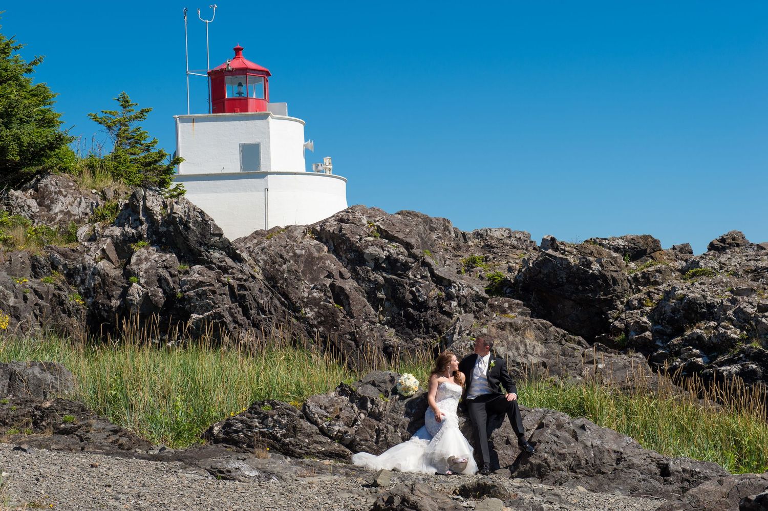 Lighthouse perched on rocky coastal cliffs under bright blue summer sky.
