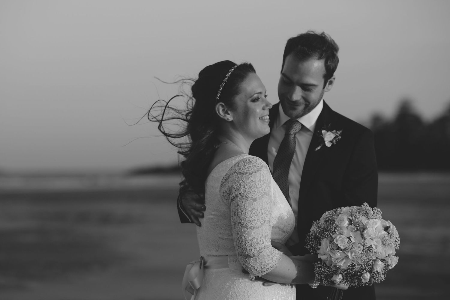 A romantic black and white portrait of newlyweds embracing with a bouquet.