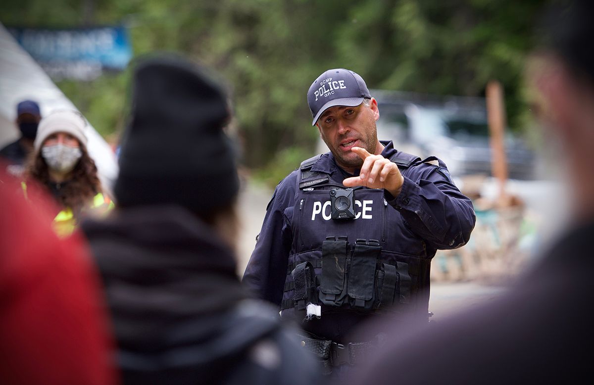 Fairy Creek blockade. Police officer in tactical gear gestures while speaking outdoors.