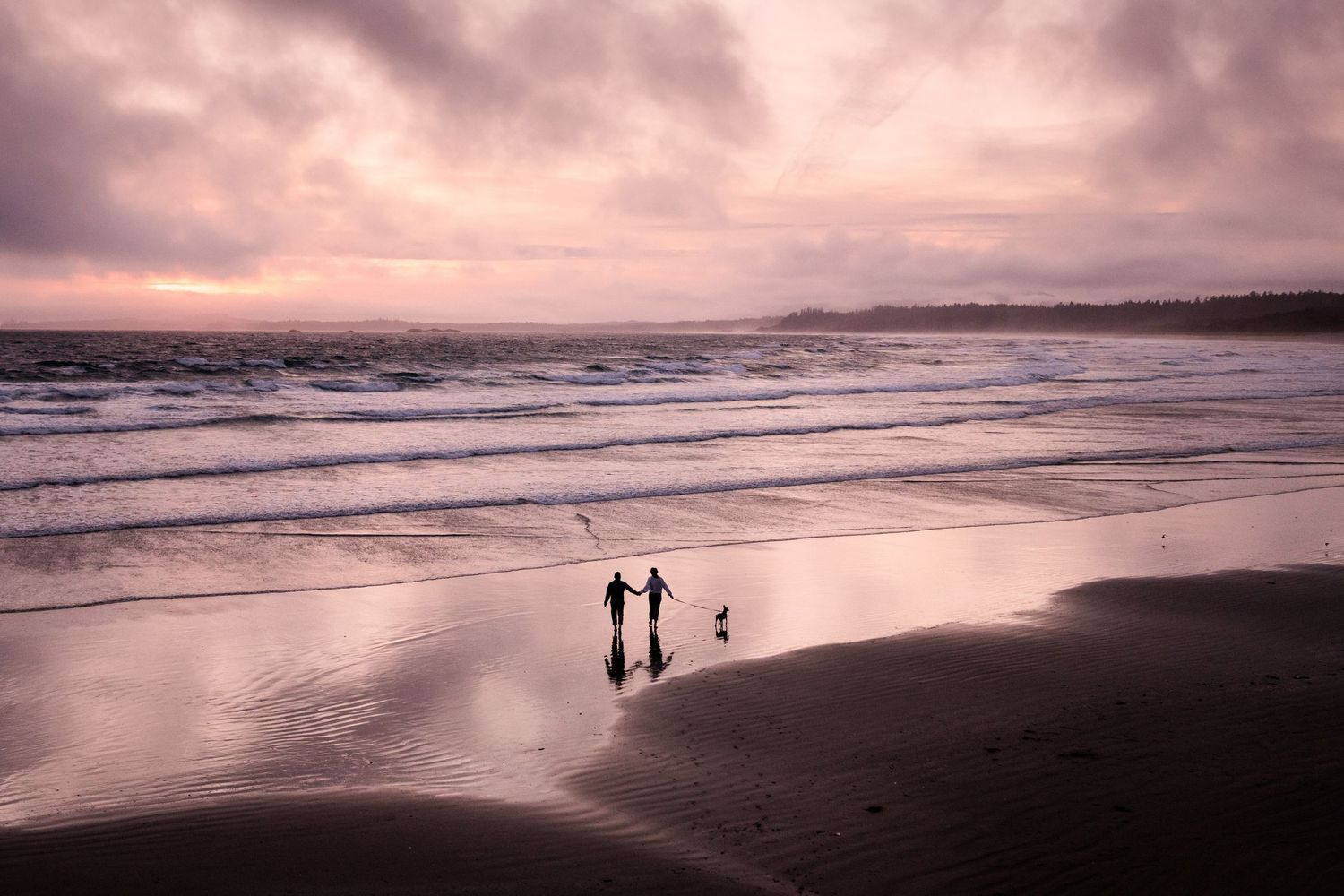 Two figures walk along a misty beach at sunset with dramatic pink clouds overhead.