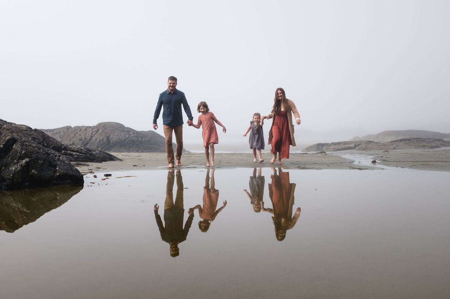 Group reflected in wet sand while exploring foggy coastal beach landscape.