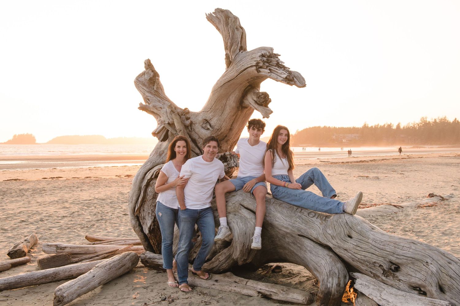 Group relaxing on driftwood at the beach during golden hour with scenic coastal views.