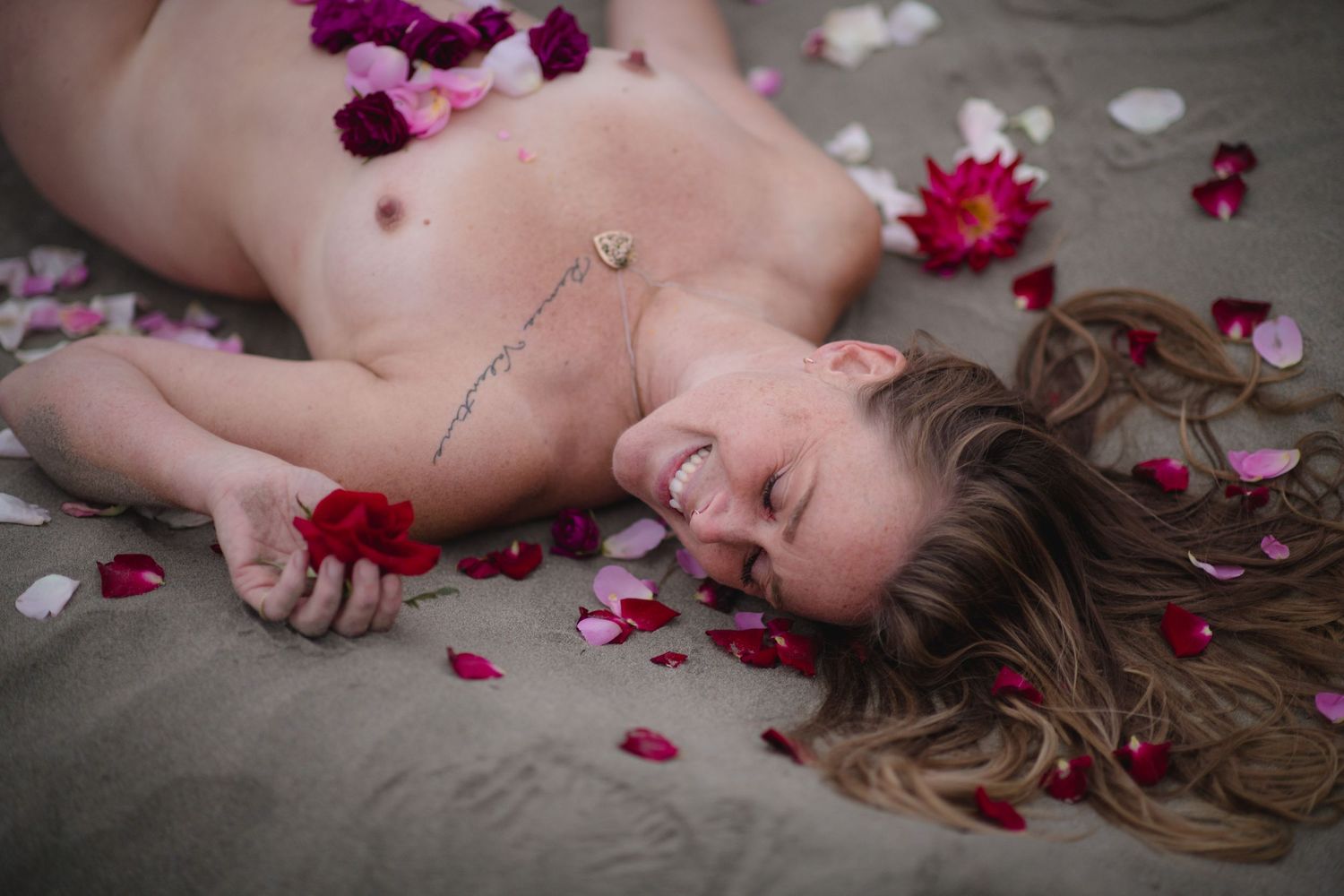 Rose petals scattered around person lying artistically on dark sand.