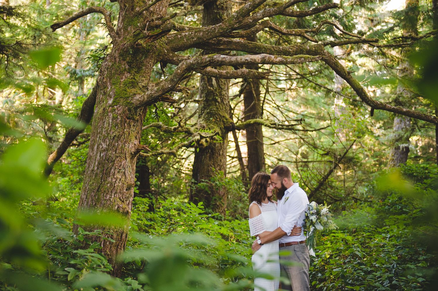 A group of people gathered outdoors under lush green trees in a natural setting.