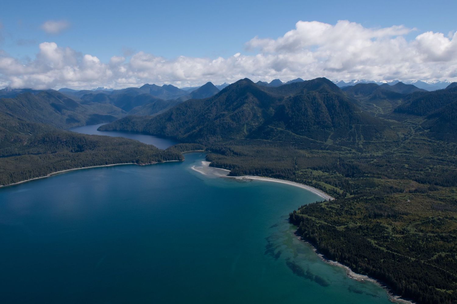 Aerial panorama of a pristine coastal bay surrounded by lush green mountains and dramatic coastline.