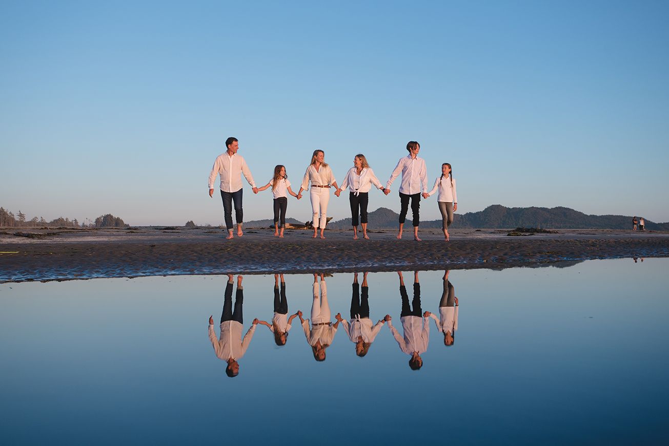 People reflected in wet sand during sunset at beach with clear blue sky.