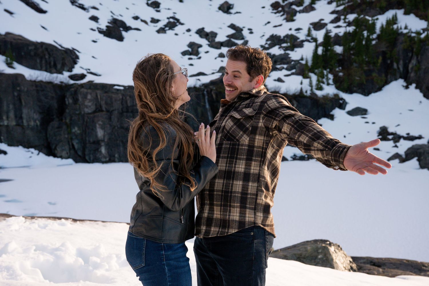 Couple laughing and dancing together in a snowy mountain landscape during a winter engagement photo session.