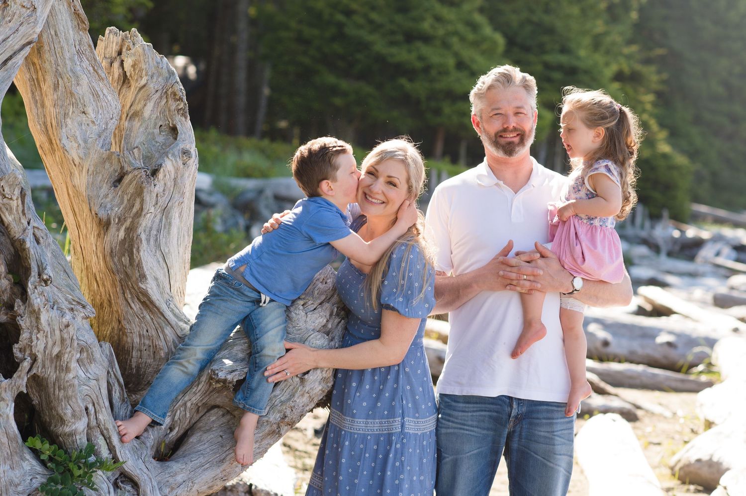 Family photo session at a scenic rocky beach with driftwood and natural coastal elements.