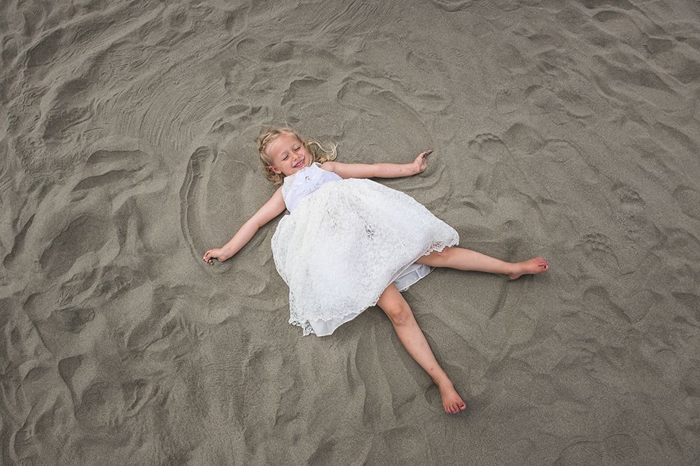 Person lying on sandy beach making sand angels.
