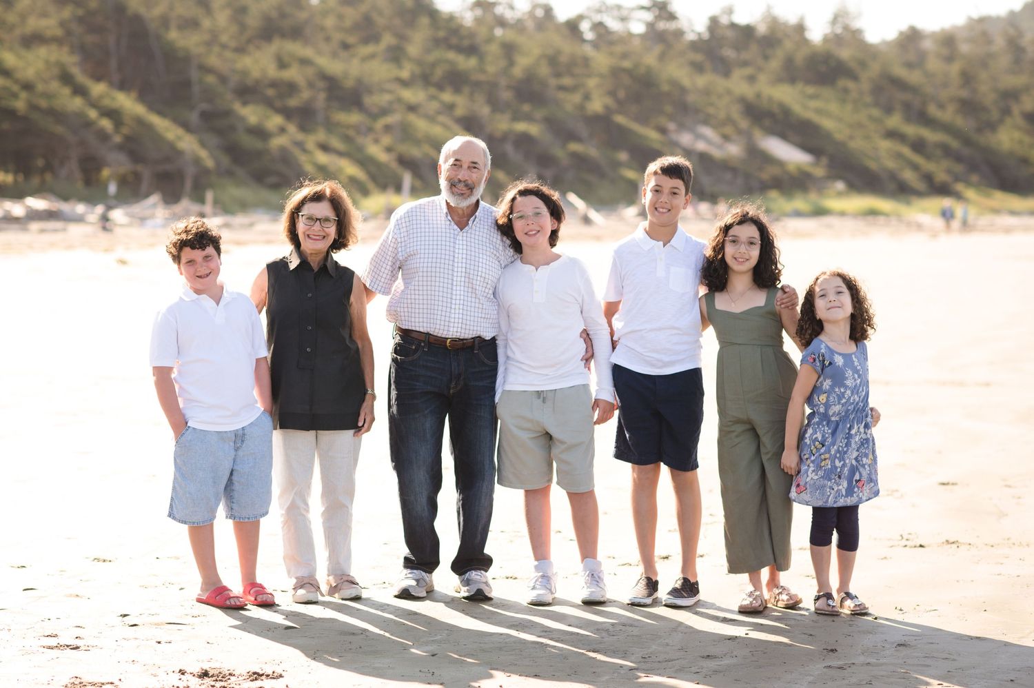 Extended family group photo session on a scenic beach with mountains in background.