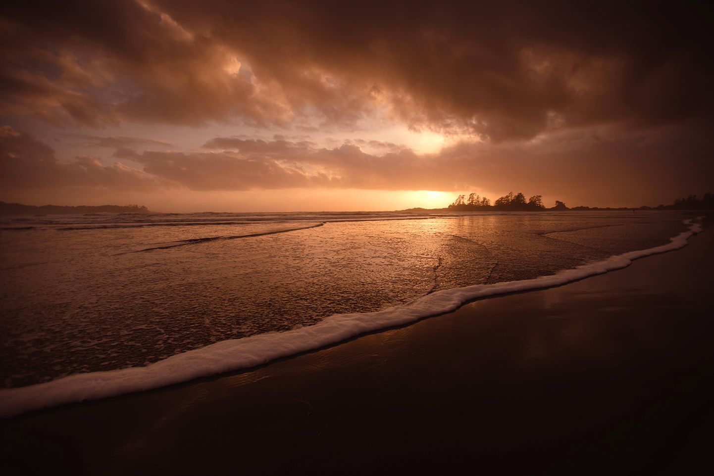 Dramatic sunset over empty beach with dark clouds and orange sky.